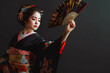 © MVProductions - Beautiful geisha in black kimono with hand fan dancing and gesturing isolated on black background, traditional Japanese woman studio shot
