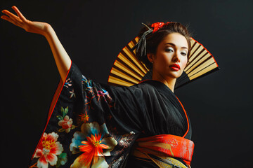 Beautiful geisha in black kimono with hand fan dancing and gesturing isolated on black background, traditional Japanese woman studio shot