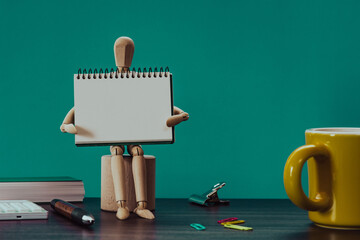 Poster - Desk with a wooden manikin sitting holding a small notebook.