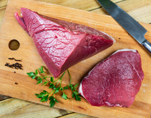 Wall Mural - Fresh, uncooked beef fillet pieces on wooden cutting board, prepared for roasting or grilling, with knife, spicy peppercorns and greens nearby..