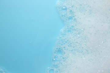 Canvas Print - Washing laundry. White foam with bubbles on light blue background, top view. Space for text