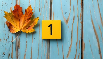 Autumn leaf and yellow number block on rustic light-blue wood, capturing simplicity, playfulness, and seasonal change