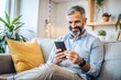 © Introvertia - Smiling elderly man using smartphone in cozy living room