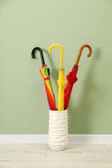 Sticker - Colorful umbrellas in holder on floor near green wall indoors