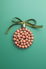 Wall Mural - Christmas ball made of cosmetic product and bow on green background, top view