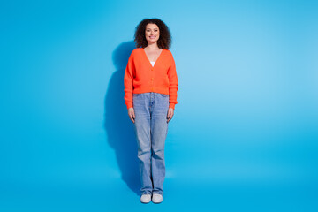 Wall Mural - Photo portrait of wavy haired model woman wearing orange cardigan and jeans stylish outfit isolated on blue color background