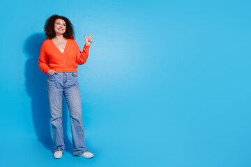 Photo portrait of chevelure hair brasil model woman wearing orange cardigan and jeans indicate finger advet isolated on blue color background