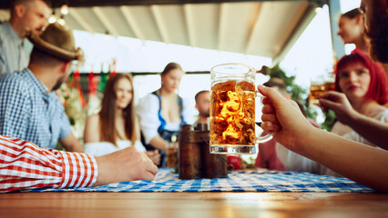 Wall Mural - Focus on lager beer mug and blurred people, friends sitting at table at bar and celebrating, drinking, talking. Concept of Oktoberfest, festival, party, brewery, traditions