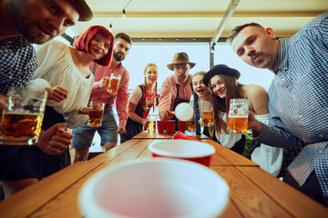 Wall Mural - Group of people cheerfully playing beer pong, having fun and bar while celebrating beer festival. Bavarian traditions. Concept of Oktoberfest, festival, party, brewery, traditions