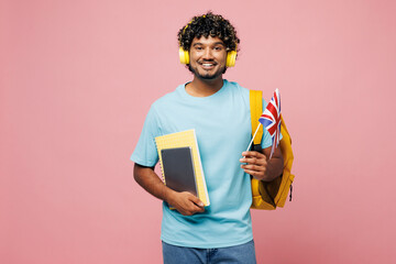 Wall Mural - Young Indian boy student wear blue t-shirt casual clothes headphones backpack bag hold book textbook British flag listen music isolated on plain pink background High school university college concept