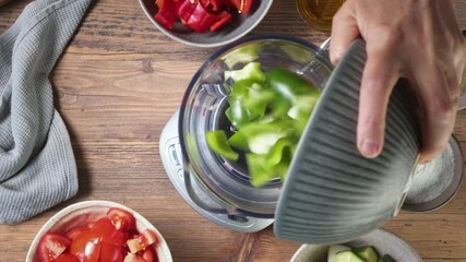 Sticker - the cook puts sliced ​​bell peppers in a blender to make healthy gazpacho soup, top view, process of making healthy meal