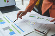 © crizzystudio - A team of businesswomen points to a strategy document with financial graphs and charts, growth, revenue, and performance of the company during an internal company meeting.