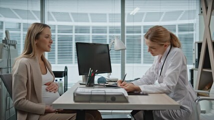 Wall Mural - Healthcare professional talking pregnant woman in office. Smiling doctor writing