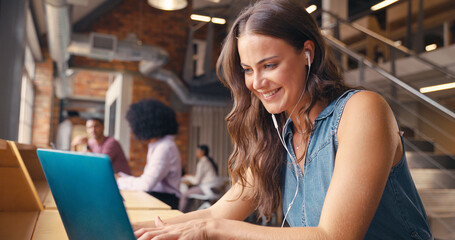 Businesswoman Working In Modern Multi-Cultural Office Listening To Music On Earphones Or Earbuds