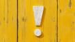 © Naru - A white exclamation mark made of wood is placed on a bright yellow wooden background. The contrasting colors create a sense of warning and attention, representing a crucial message or important announ