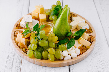 Round wooden platter presenting cheese selection with grapes and pear