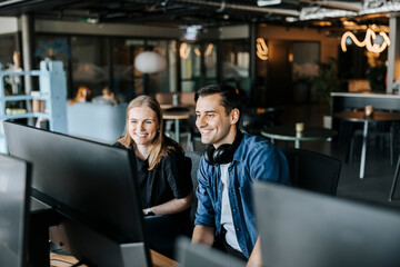 Happy male and female entrepreneurs watching computer screen sitting in tech startup office