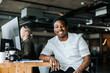 © Maskot - Portrait of smiling young entrepreneur with tattooed arm sitting at desk in office