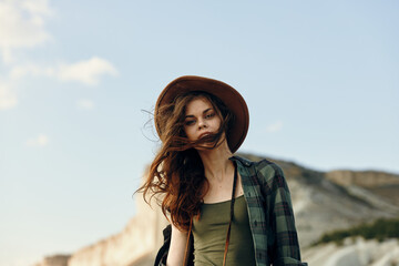 Wall Mural - serene woman in hat and plaid shirt enjoys the scenic view of mountains on a peaceful beach