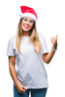 © Krakenimages.com - Young beautiful woman wearing christmas hat over isolated background smiling with happy face looking and pointing to the side with thumb up.