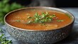 © Yuliia - a bone broth bowl with a rich, golden color, a few floating herbs for garnish, and steam rising gently, set against a simple, neutral background