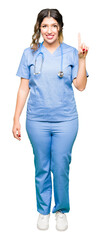 Wall Mural - Young adult doctor woman wearing medical uniform showing and pointing up with finger number one while smiling confident and happy.