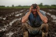 © Milos - A frustrated farmer sits with his hands on his head in a muddy field, showing signs of distress and exhaustion, possibly due to crop failure or adverse weather conditions.