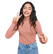 © Krakenimages.com - Hispanic teenager girl with dental braces wearing casual clothes smiling looking to the camera showing fingers doing victory sign. number two.
