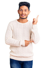 Handsome latin american young man wearing casual winter sweater smiling happy pointing with hand and finger to the side