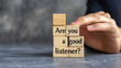 © Best_Seller - A businessman's hand holds wooden blocks spelling 'Are you a good listener?' against a grey background. This image highlights the importance of listening skills in business.