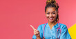 © Bartek - Smiling Young African American Nurse with Braids Pointing to the Side Isolated on Colorful Background Wearing Blue Scrubs and Pink Stethoscope, Professional Healthcare Concept