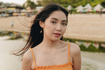 Elegant young Asian woman in a yellow dress is striking a pose by the beach.