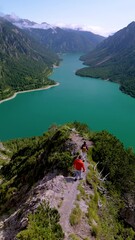 Wall Mural - Plansee Austria, A stunning landscape with a serene turquoise lake surrounded by majestic mountains and adventurous hikers. a couple of man and woman hiking to the top of Plansee Austria Tyrol