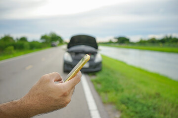 Wall Mural - Close-up of male driver's hand holding a smartphone calling mechanic with a broken car on the side of the road.