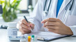 © TinyUU - Doctor writing a prescription with medication bottles on the desk.