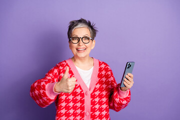 Wall Mural - Photo portrait of cute senior woman thumb up hold device dressed stylish red clothes isolated on violet color background