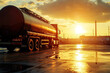 © Kitta - A lone tanker truck stands at a loading station, silhouetted against a breathtaking sunset, the golden light reflecting in puddles on the wet asphalt.