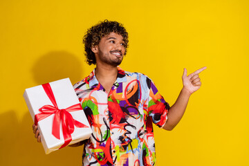 Sticker - Photo of attractive young man hold gift point look empty space dressed stylish colorful clothes isolated on yellow color background