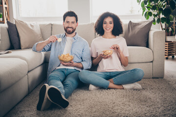 Sticker - Full size photo of two nice young partners eat chips sit floor weekend modern apartment indoors