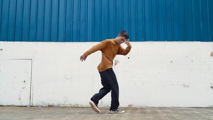 Wall Mural - Hispanic man stretch arms and dance street dancing in front of wall. Motion shot of stylish dancer or choreographer in casual outfit practicing dancing in hip hop style. Outdoor sport 2024. Hiphop.