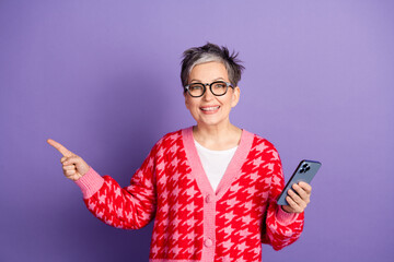 Poster - Photo portrait of lovely pensioner lady hold gadget point empty space dressed stylish red garment isolated on violet color background