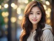 © vladrom - A young asian woman with long dark hair, looking at the camera with a gentle smile. Close-up. She is wearing a light beige shirt and is standing in front of a blurred background of green plants
