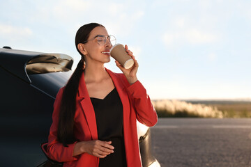 Wall Mural - Beautiful young woman drinking from paper cup near car outdoors, space for text