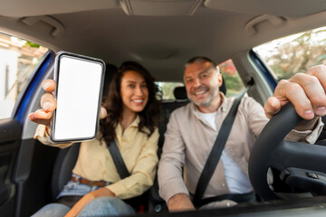 Car rental app. Happy spouses showing blank smartphone screen for application or website mockup while sitting in auto and smiling