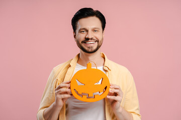 Smiling man holding halloween pumpkin decoration on pink background