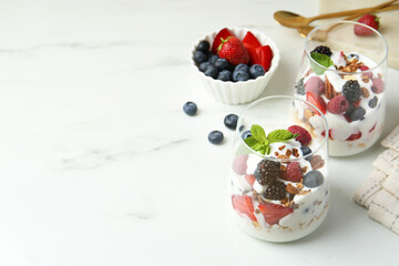 Poster - Tasty yogurt with fresh berries, granola and mint in glasses on white marble table, space for text