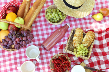 Wall Mural - Picnic wicker baskets with delicious food, tableware and drink on checkered tablecloth, flat lay