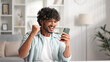 © YURII MASLAK - Satisfied Indian man checking his email and happy with good news. A young man winner celebrating the victory sitting at the table, raises his hands uphill.