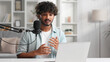 © YURII MASLAK - Microphone, podcast and Indian man speaker in his living room. Creative streamer, internet influencer or online content creator live streaming for audience.