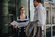 © qunica.com - Two professional colleagues engaging in a discussion about project plans in front of a modern glass office building, conveying teamwork and business collaboration.
